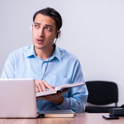 man reading book with a blue shirt on and a laptop